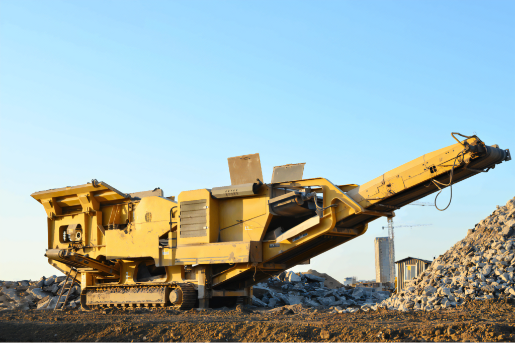 Kruszarka szczękowa pracująca na placu budowy, z dużym stosem kruszywa w tle.