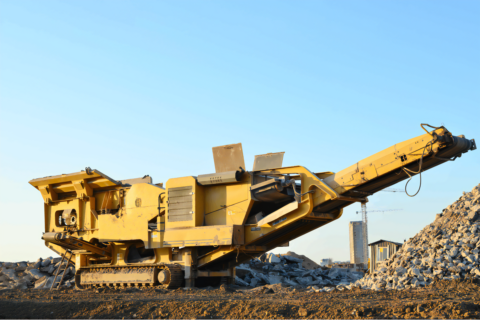 Kruszarka szczękowa pracująca na placu budowy, z dużym stosem kruszywa w tle.