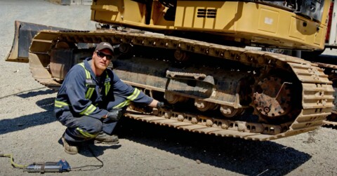 Mechanik w odzieży roboczej, klęczący obok gąsienicy maszyny budowlanej, sprawdzający system podwozia.