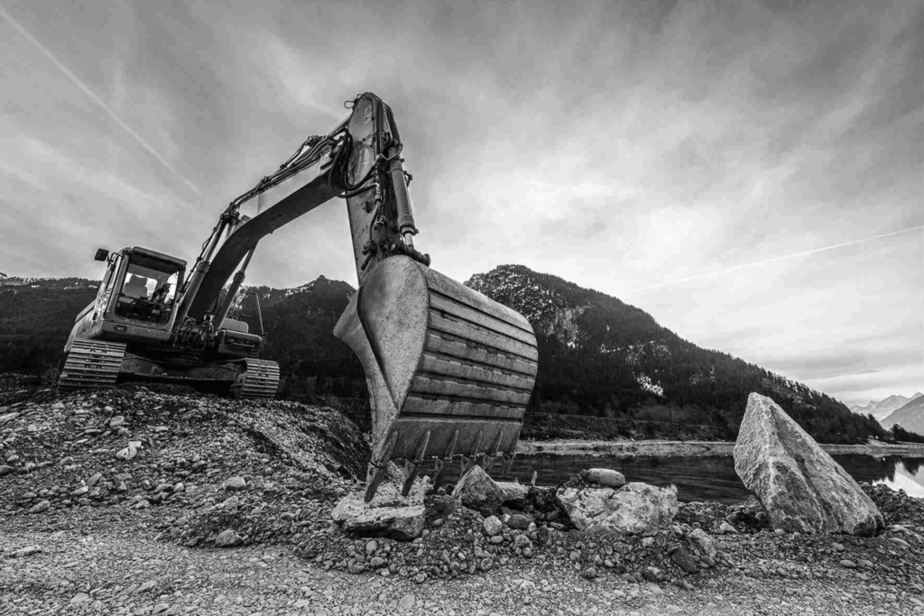 Czarno-białe zdjęcie koparki pracującej na kamienistym terenie.