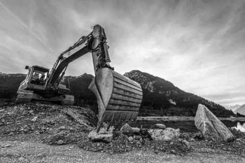 Czarno-białe zdjęcie koparki pracującej na kamienistym terenie.