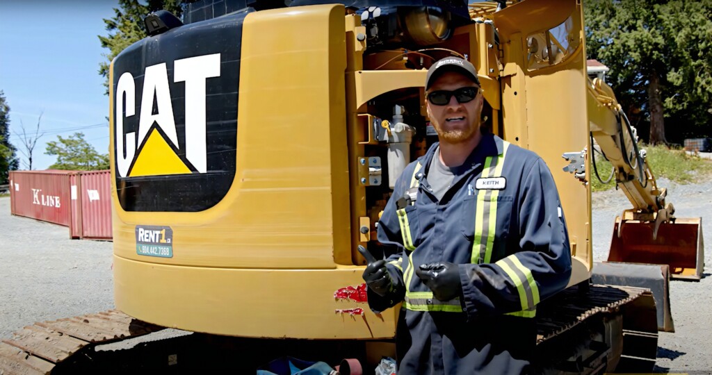 Mężczyzna w odzieży roboczej stojący przed maszyną budowlaną marki CAT.