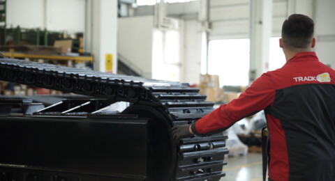 Pracovník kontrolující pásový podvozek ve výrobní hale.