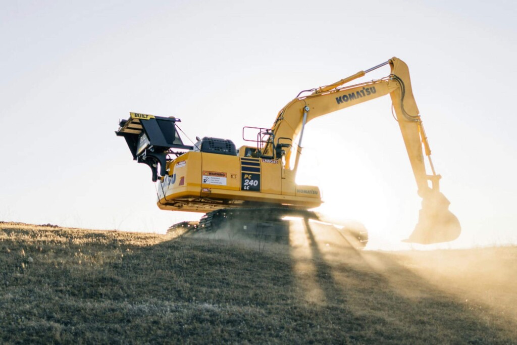 Rypadlo Komatsu PC240 LC pracující na kopci při východu slunce.