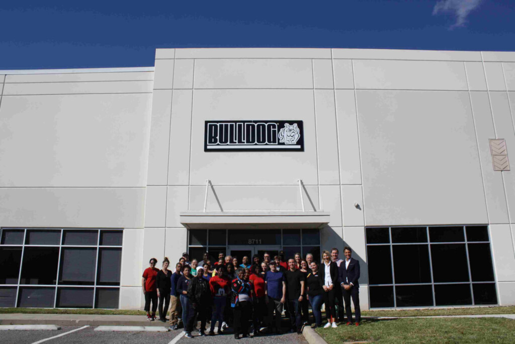 Skupina lidí stojící před budovou s logem BULLDOG.