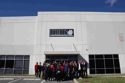Skupina lidí stojící před budovou s logem BULLDOG.