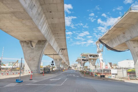 Konstrukce mostu během výstavby, s viditelnými pilíři a částečně dokončenými úseky mostu.