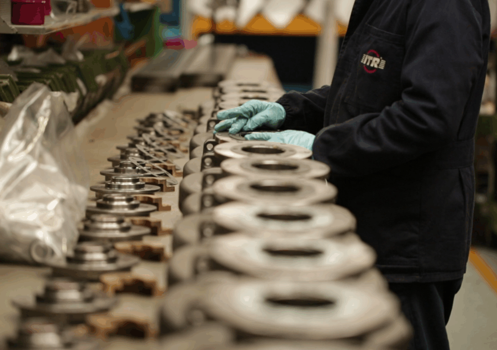 Pracovník v tmavém pracovním oděvu a rukavicích skládá kovové díly.