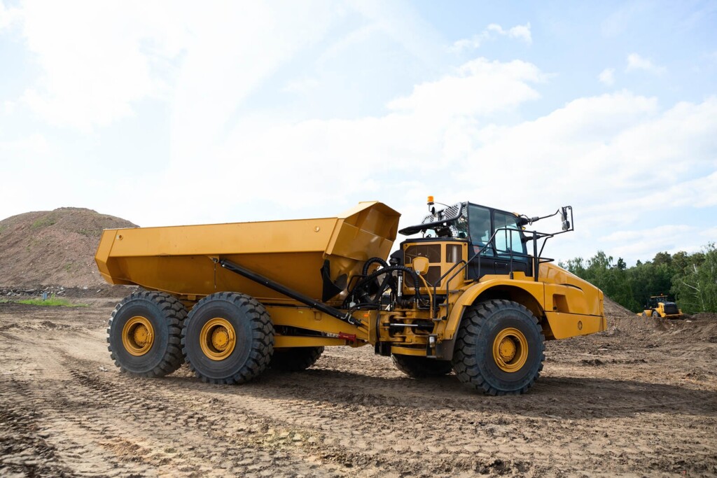 Žluté stavební sklápěcí vozidlo stojí na staveništi, na pozadí je zemní kopec.