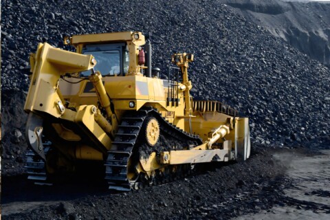 Žlutý pásový buldozer pracující na velké hromadě uhlí.