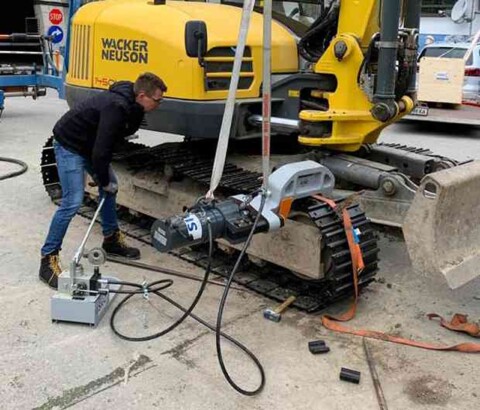 Pracovník obsluhující ruční hydraulickou lis při žluté minirypadle značky Wacker Neuson.