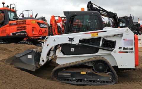 Kompaktní pásová nakladačka Bobcat T450 pracující na staveništi, v pozadí stavební stroje značky Doosan.