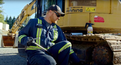 Mechanik v pracovním oděvu s nářadím v ruce opravuje stavební stroj značky CAT.