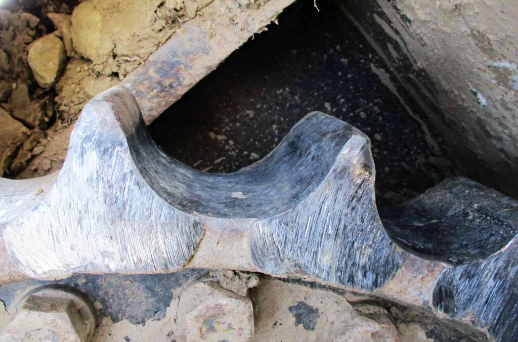 Detailní pohled na opotřebovaný hnací pastorek v podvozku stavebních strojů.